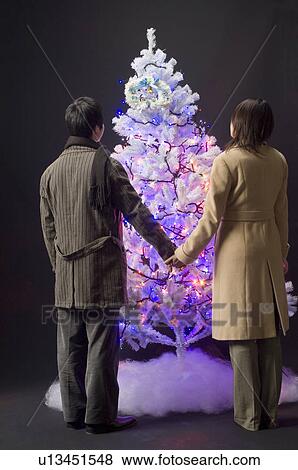 Couple standing in front of Christmas tree View Large Photo Image Stock Photo - Couple standing in front of Christmas tree. Fotosearch