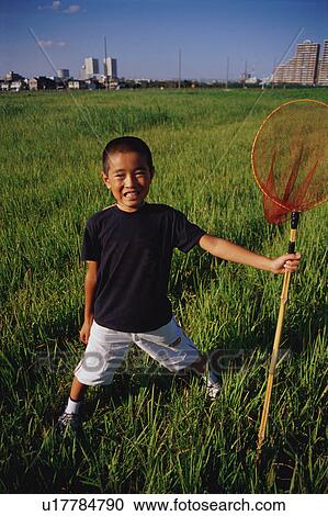 Stock Image - Boy standing in field with butterfly net. Fotosearch