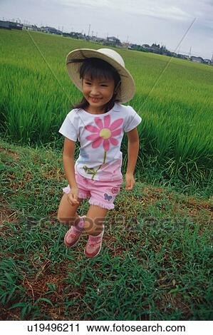 Stock Image - Girl jumping in front of rice paddy. Fotosearch