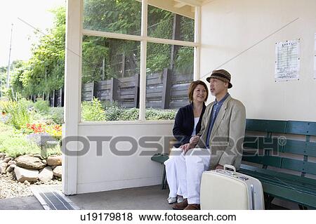 Stock Photo - Senior couple sitting on bench at station. Fotosearch