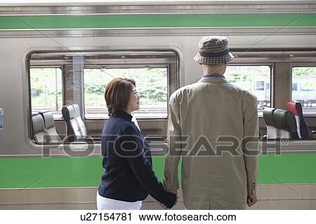 Stock Image - Senior couple standing in front of train. Fotosearch
