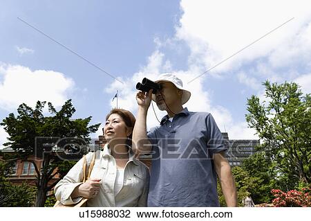 Stock Image - Senior couple standing, man using binoculars. Fotosearch