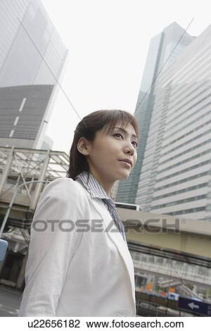 Stock Image - A low angle view of a woman with commercial buildings at the background. Fotosearch