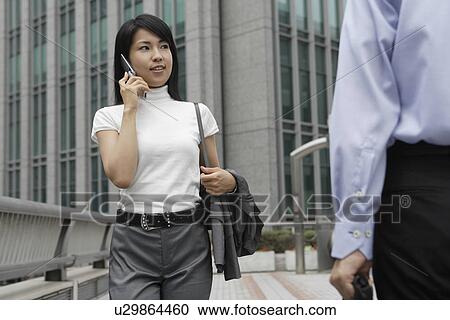 Stock Image - A professional woman converses on the mobile phone as she moves. Fotosearch