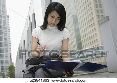 A woman holding a pen looks over the documents in a file View Large Photo Image Stock Image - A woman holding a pen looks over the documents in a file. Fotosearch