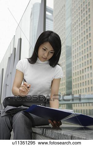 Stock Photography - A woman holding a pen looks over the documents in a file. Fotosearch