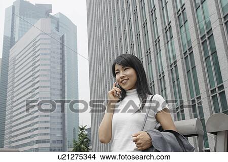 Picture - A woman seen conversing on the mobile phone amidst a commercial area. Fotosearch