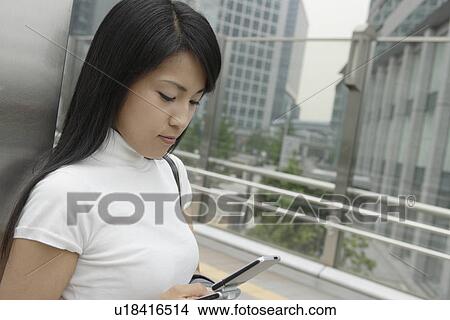 A woman standing at a side as she looks over her mobile phone View Large Photo Image Picture - A woman standing at a side as she looks over her mobile phone. Fotosearch