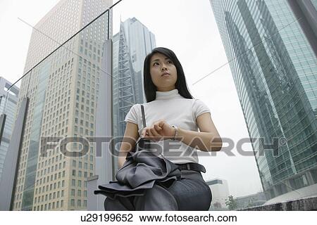 Stock Image - A woman waiting for someone as she is seated near a commercial area. Fotosearch