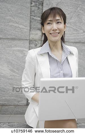 Stock Photograph - A woman working on her laptop smiles at someone. Fotosearch