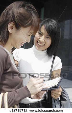 Stock Image - Two women exchanging laughter as they look over a diary. Fotosearch