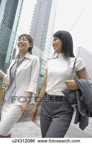 Two women laughing as they walk beside the glass railing View Large Photo Image Stock Photograph - Two women laughing as they walk beside the glass railing. Fotosearch