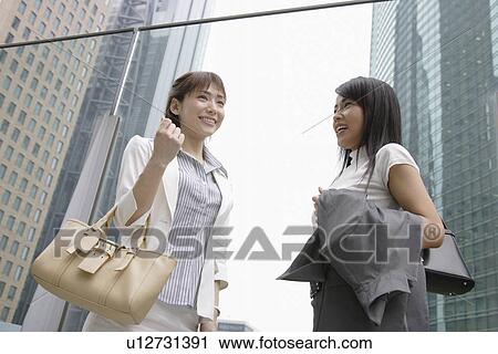 Stock Image - Two women shares a joke standing beside the glass railing. Fotosearch