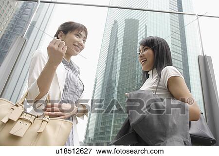 Stock Photo - Two women shares a joke standing beside the glass railing. Fotosearch