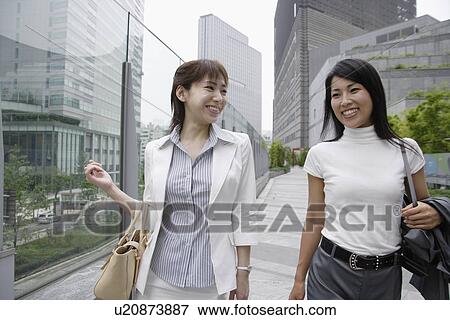 Stock Photo - Two women shares a joke walking beside the glass railing. Fotosearch