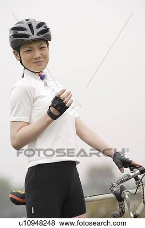 Stock Photo - Close-up of a young woman standing near her bicycle. Fotosearch