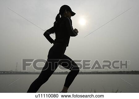 View of a young woman jogging beside a river View Large Photo Image Stock Image - View of a young woman jogging beside a river. Fotosearch
