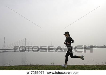 View of a young woman jogging beside a river View Large Photo Image Stock Image - View of a young woman jogging beside a river. Fotosearch