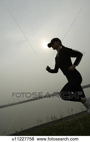 View of a young woman jogging beside a river View Large Photo Image Stock Photo - View of a young woman jogging beside a river. Fotosearch