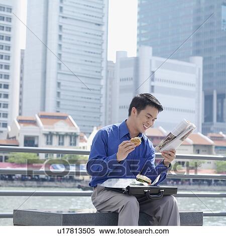 Businessman eating a burger and reading a magazine on a pier View Large Photo Image Stock Photography - Businessman eating a burger and reading a magazine on a pier. Fotosearch