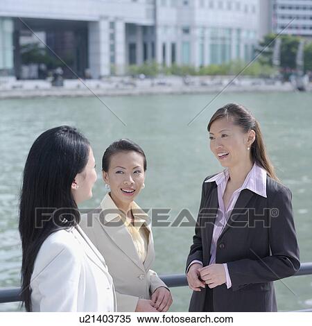 Stock Photography - High angle view of three businesswomen smiling at each other. Fotosearch