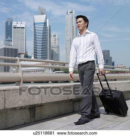 Stock Image - Low angle view of a businessman pulling a suitcase. Fotosearch