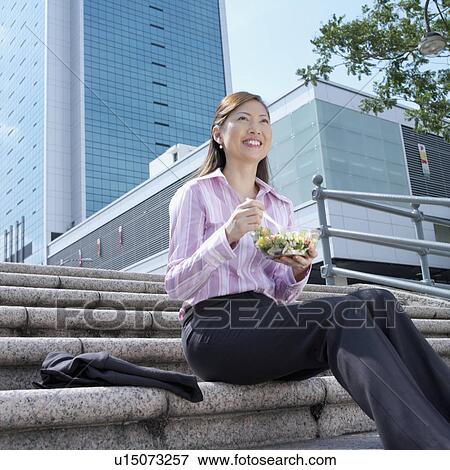 Stock Photo - Low angle view of a businesswoman holding a bowl of salad. Fotosearch