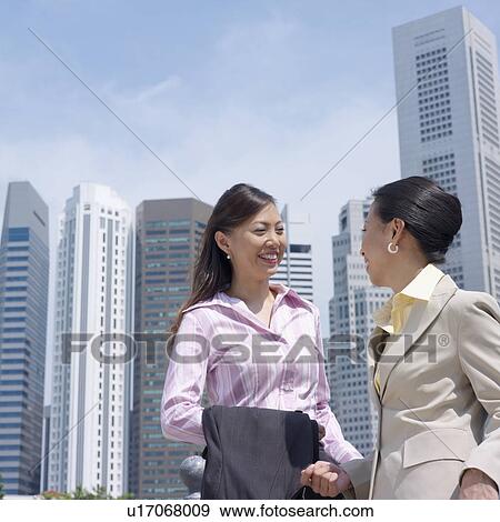 Stock Photo - Low angle view of two businesswomen smiling at each other. Fotosearch