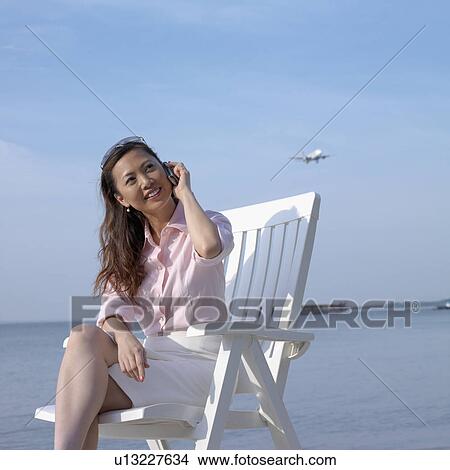 Picture - Mid adult woman talking on a mobile phone at the beach. Fotosearch
