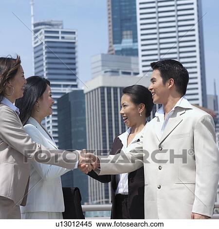 Side profile of a businessman and a businesswoman shaking hands with their colleagues View Large Photo Image Stock Photography - Side profile of a businessman and a businesswoman shaking hands with their colleagues. Fotosearch