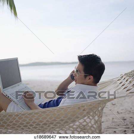 Stock Photo - Side profile of a mid adult man lying in a hammock talking on a mobile phone. Fotosearch