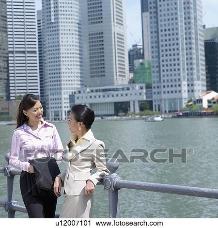 Stock Image - Two businesswomen leaning against a railing. Fotosearch