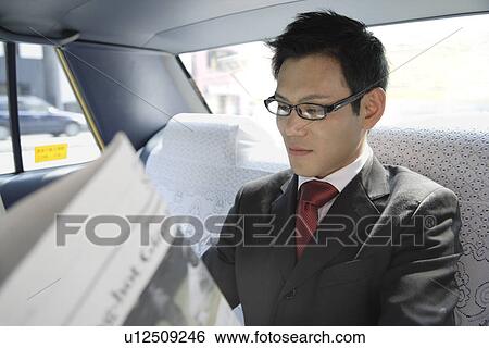 Stock Photograph - Businessman reading a newspaper in a car, portrait. Fotosearch