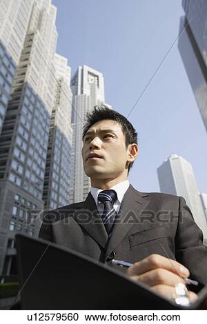 Stock Image - Businessman with office buildings, portrait. Fotosearch