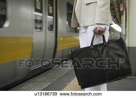 Woman holding a bag at a railroad station View Large Photo Image Stock Photo - Woman holding a bag at a railroad station. Fotosearch