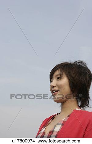Picture - A young woman is seen under the sky as she smiles heartily. Fotosearch