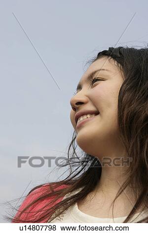 A young woman is seen under the sky as she smiles heartily View Large Photo Image Stock Photo - A young woman is seen under the sky as she smiles heartily. Fotosearch