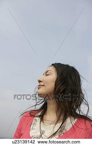 Stock Image - A young woman is seen under the sky with her eyes closed. Fotosearch