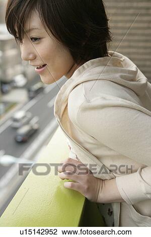 A young woman leans against the railing of the balcony as she looks down at the street View Large Photo Image Stock Image - A young woman leans against the railing of the balcony as she looks down at the street. Fotosearch