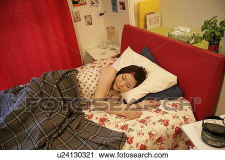 Stock Image - A young woman sleeps peacefully on the bed in a cozy bedroom. Fotosearch