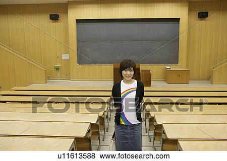 Stock Photo - A young woman stands alone inside the classroom as she smiles at the camera. Fotosearch