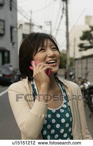 Stock Image - A young woman stands in the middle of the road while she talks on the cell phone. Fotosearch