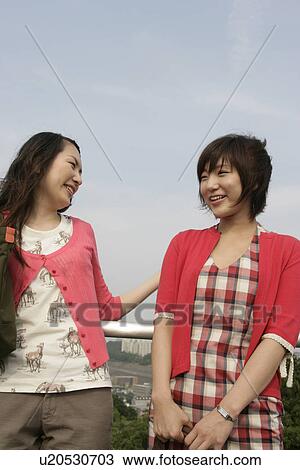 Stock Image - Two young women heartily share laughter as they stand against the railing. Fotosearch