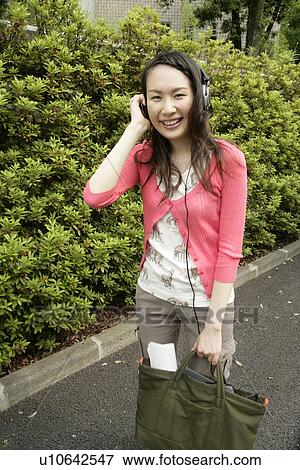 Young woman stands with her handbag while she puts her headphones on and listens to the music View Large Photo Image Stock Photo - Young woman stands with her handbag while she puts her headphones on and listens to the music. Fotosearch