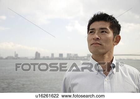 Stock Image - View a young man looking away with sea in background. Fotosearch