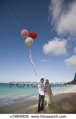 Stock Photography - A young couple holding balloons at beach. Fotosearch