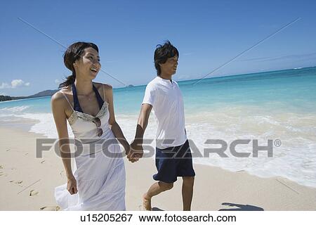 Stock Photo - A young couple holding hands at beach. Fotosearch