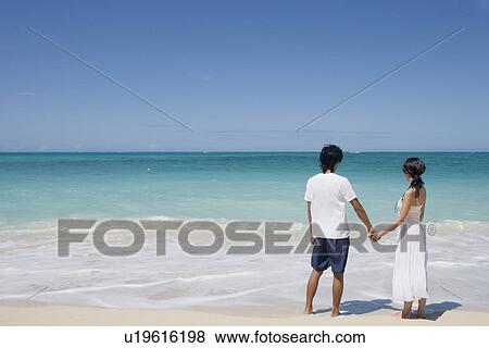 Stock Photo - A young couple holding hands at beach. Fotosearch