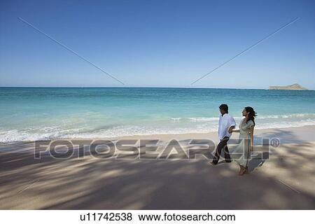 Stock Photo - Elevated view of a young couple walking at beach. Fotosearch