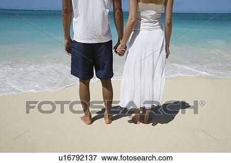 Lo section of a couple holding hands at beach View Large Photo Image Stock Photo - Lo section of a couple holding hands at beach. Fotosearch